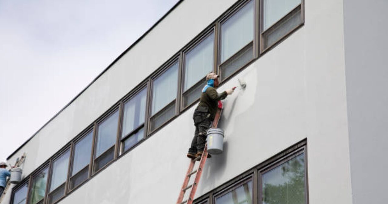 Worker applying white paint to a multi-story building exterior during a commercial and industrial painting services