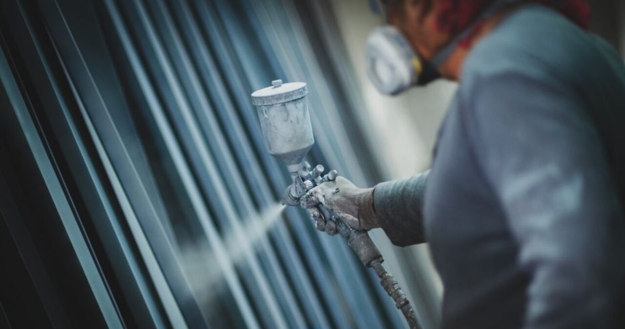 Industrial painter spray-applying a protective coating to metal structures, crucial for preventing paint fading and corrosion.