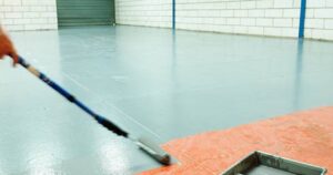 A professional painter applying a new floor coating, a key part of a comprehensive Warehouse Paint Renewal to improve durability and appearance.