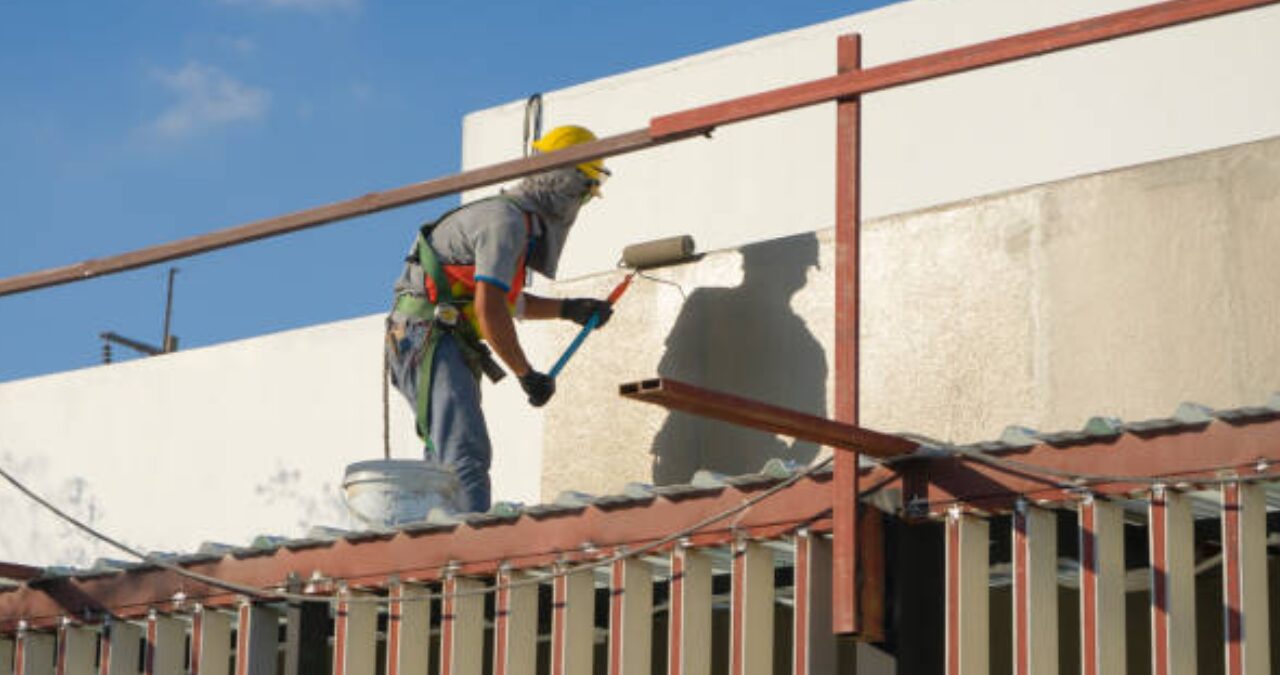 Worker repainting exterior wall of commercial property showing signs a commercial building need repainting