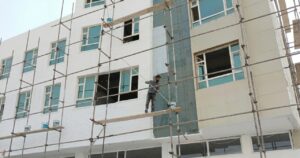 A commercial painter applying exterior coating on scaffolding alongside a multi-story building — illustrating the professional crew work required to minimize downtime during a commercial painting project.