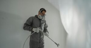 A professional painter in protective gear spray-applying a commercial interior coating — the kind of efficient, safety-compliant execution that helps minimize downtime during a commercial painting project.