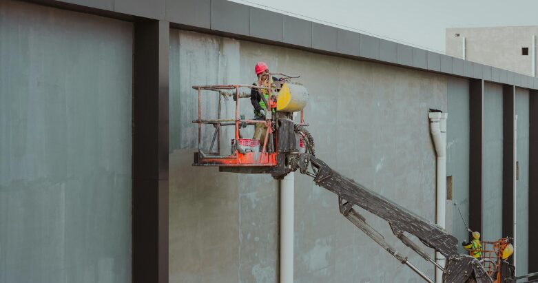 Commercial painting crew using a red boom lift to apply exterior coatings to a large warehouse in Chattanooga, TN.