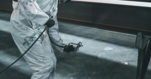 Close up of a commercial painter in a white protective suit holding a spray gun tool in an industrial facility.