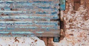 Corroded corrugated metal siding with peeling blue paint on a Chattanooga industrial building requiring rust-inhibitive coatings.