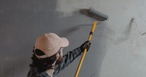 A commercial painter using an extension roller to apply gray paint to an interior wall of a Chattanooga facility.