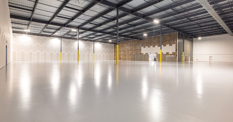 A massive, empty commercial warehouse showcasing a freshly completed, high-gloss light gray epoxy floor coating reflecting overhead lighting.