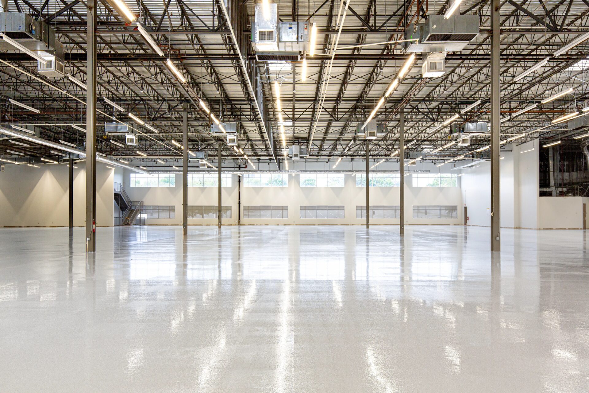 Large empty warehouse with high-gloss epoxy floor coating exposed steel trusses and industrial lighting in a commercial facility