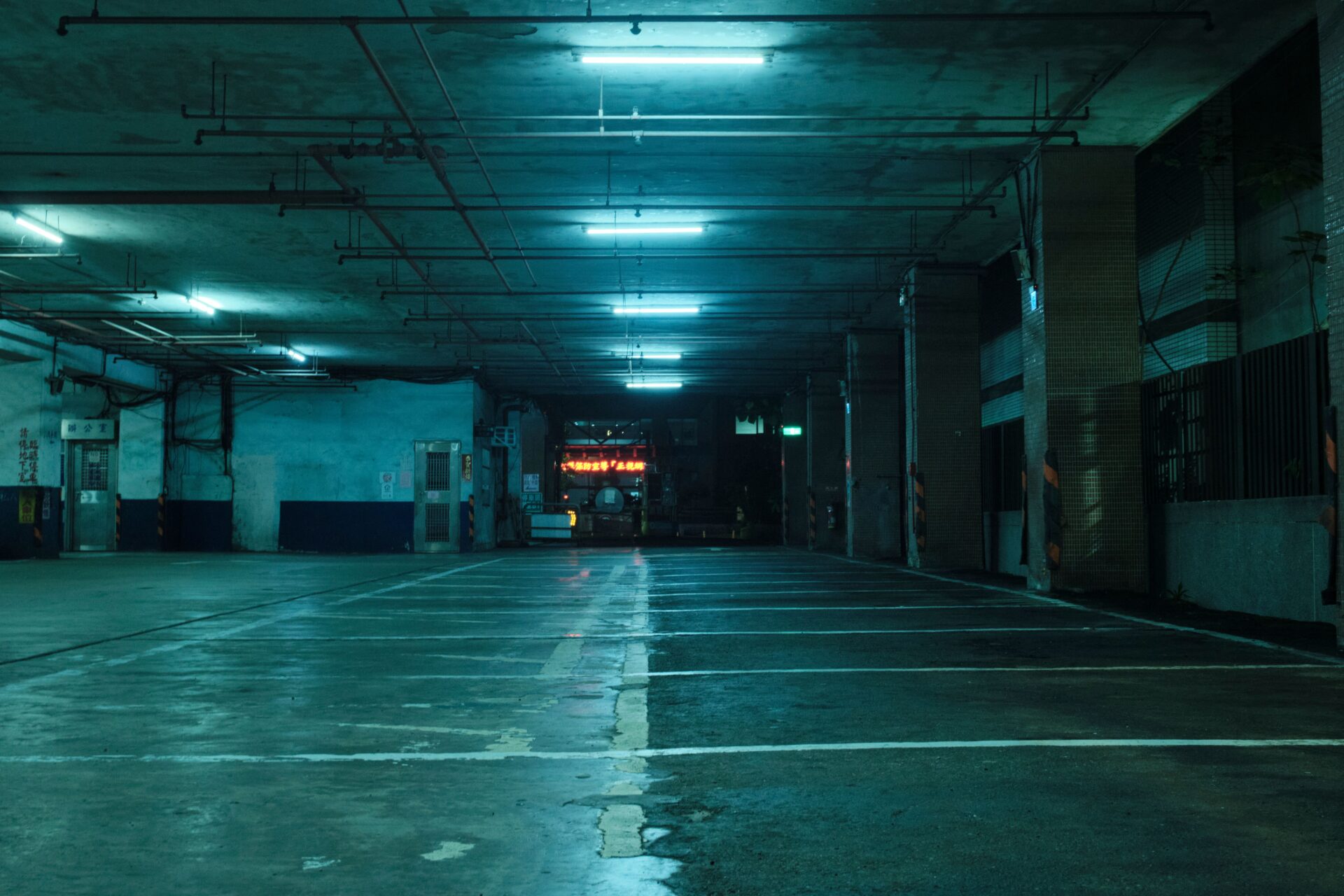 Aging underground parking garage with worn uncoated concrete floor surface moisture stains and exposed ceiling utilities showing need for traffic coating