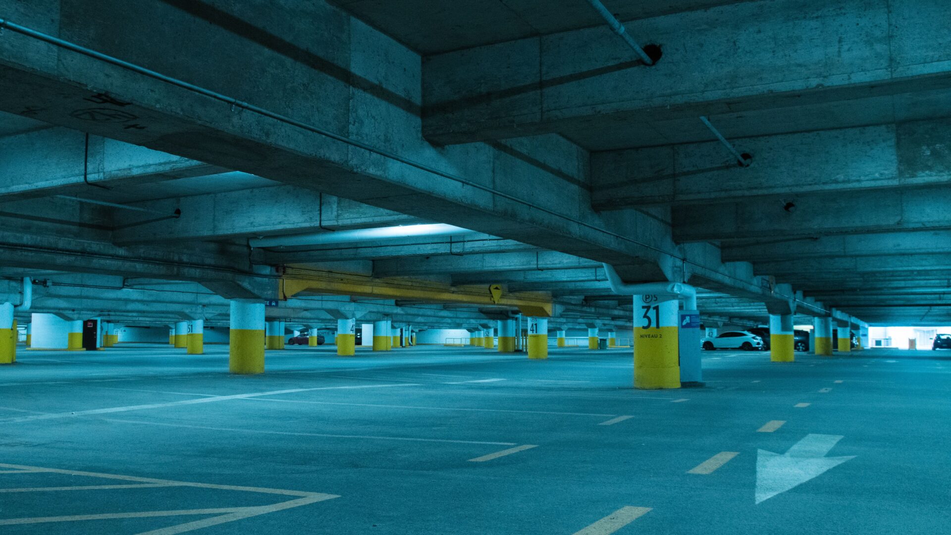 Multi-level concrete parking garage interior with exposed structural beams bare concrete deck and yellow-painted columns ready for traffic coating application