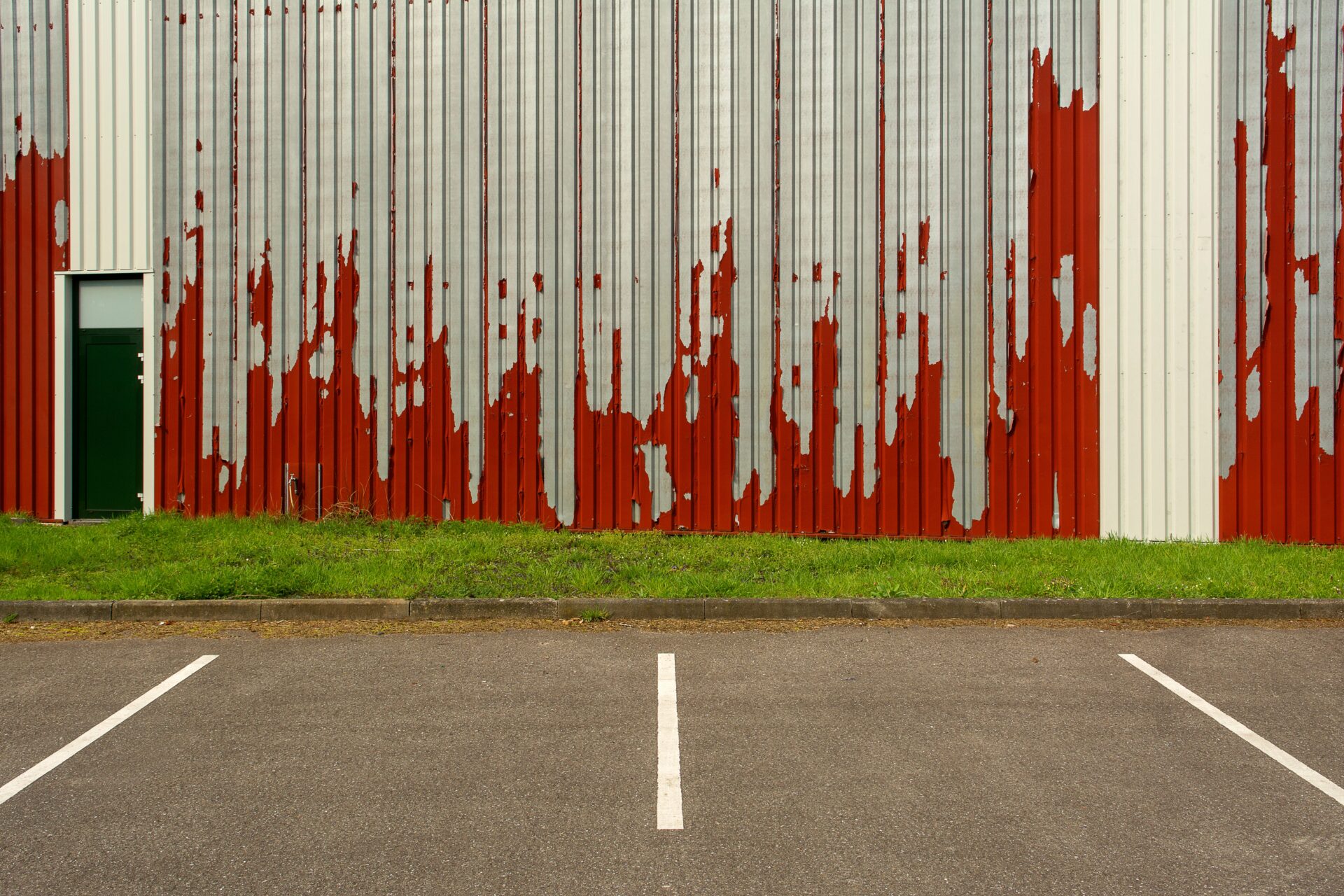 Severely peeling red paint on a commercial metal building exterior showing coating failure caused by weather exposure