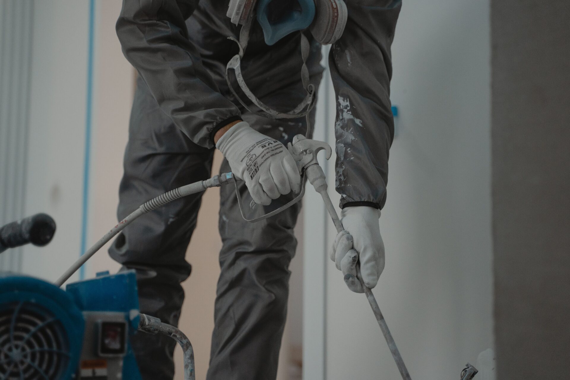 Commercial painting contractor in protective coveralls operating airless spray equipment to apply coatings after surface preparation