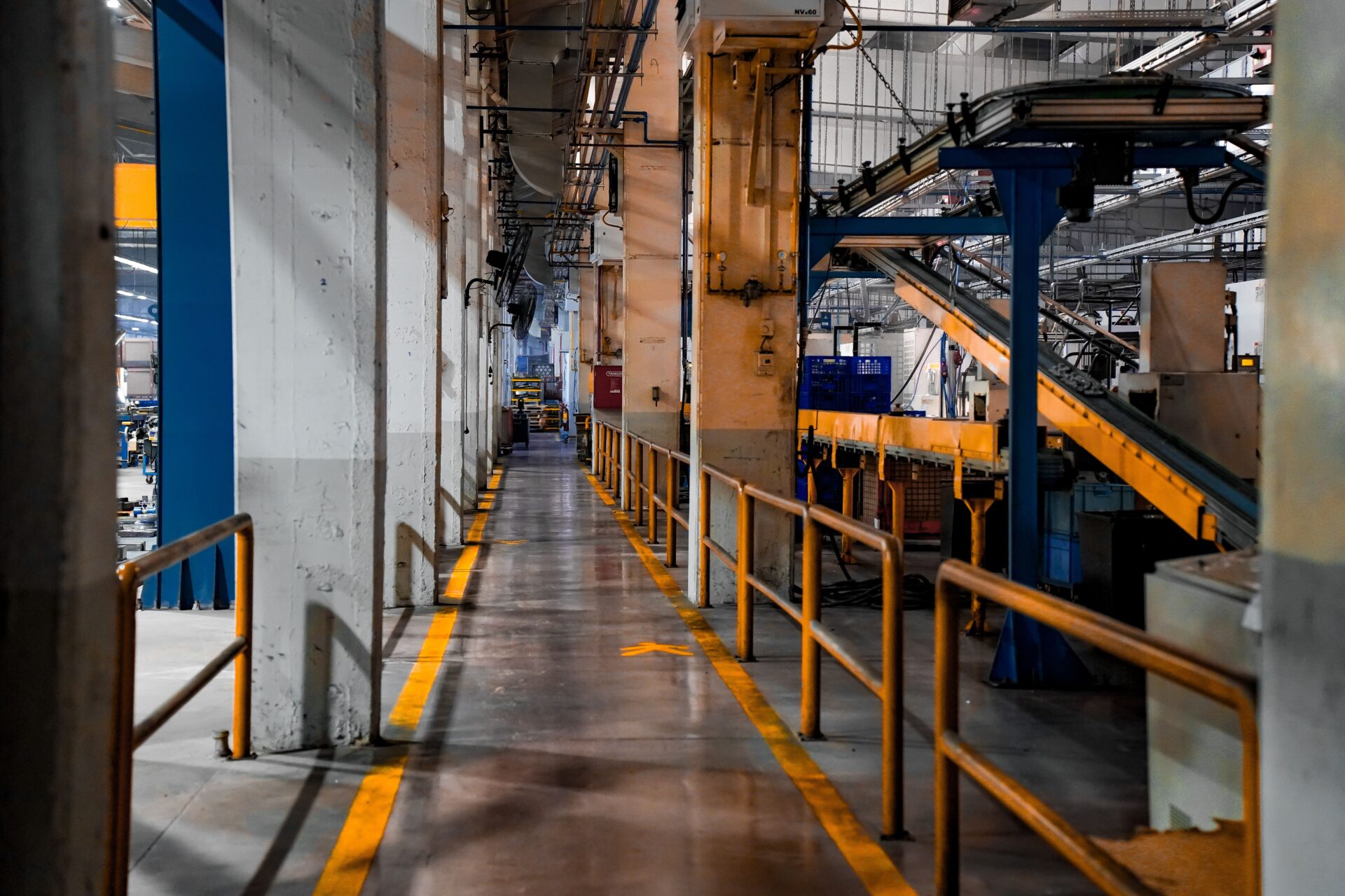 Manufacturing plant walkway with yellow safety striping on an industrial floor coating showing wear from heavy daily equipment and foot traffic